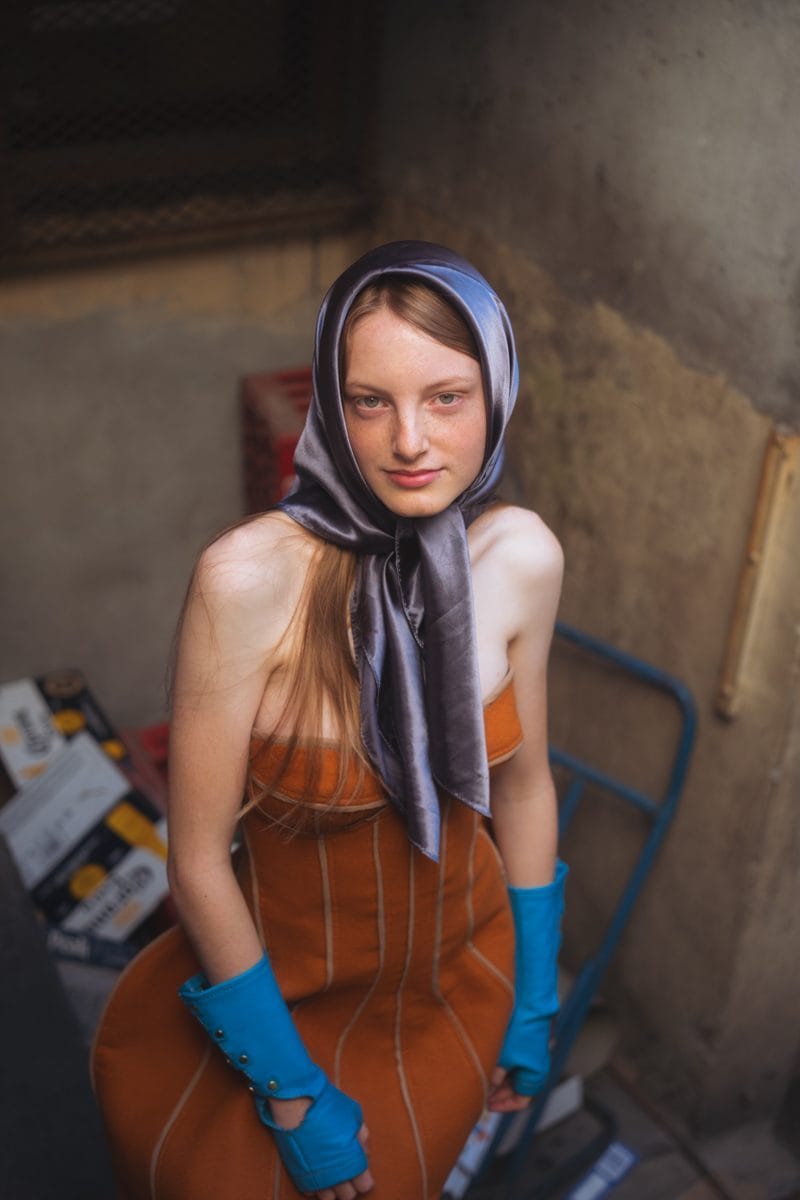 Seated portrait in the back room of the shop, lilac headscarf and rust corset dress