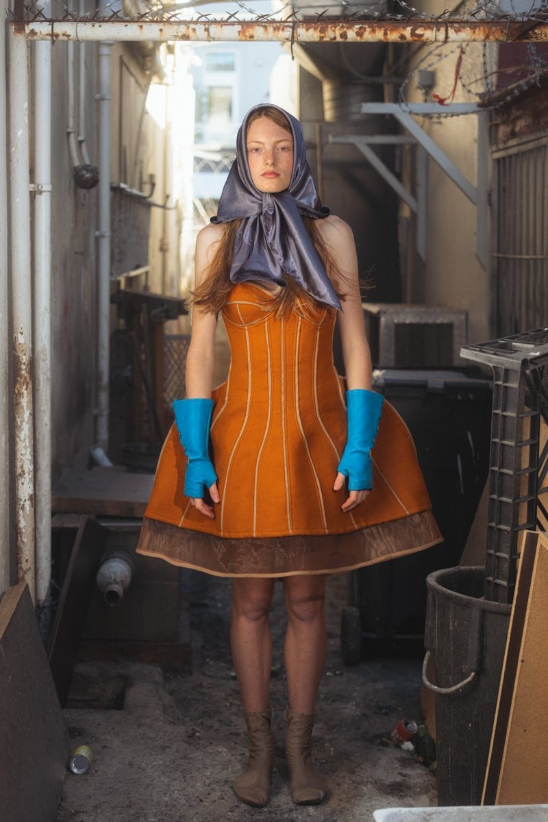 Model standing in the alleyway behind Kiosk, Cape Town, in a rust corset dress and blue gloves