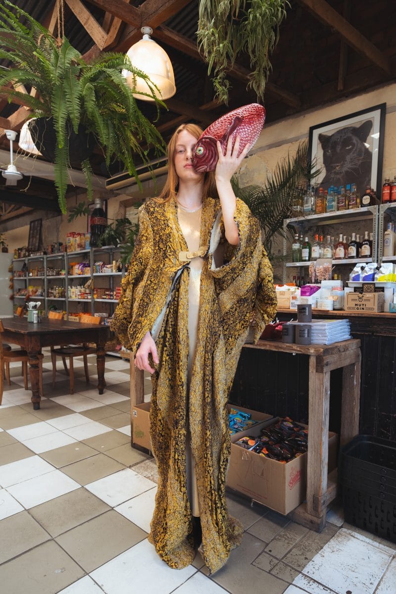 Model holding a large red fish beside her face in the middle of the shop, gold brocade coat
