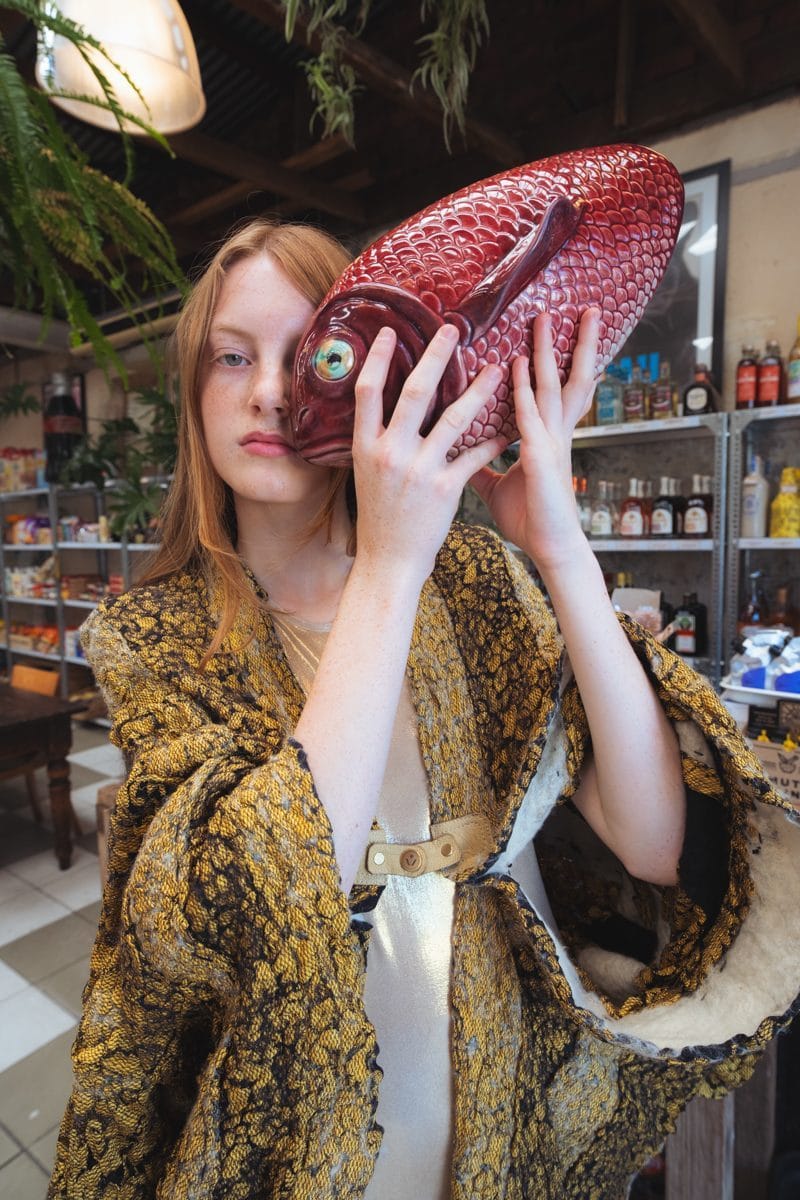 Close portrait, a large red fish held in front of the face, gold brocade coat