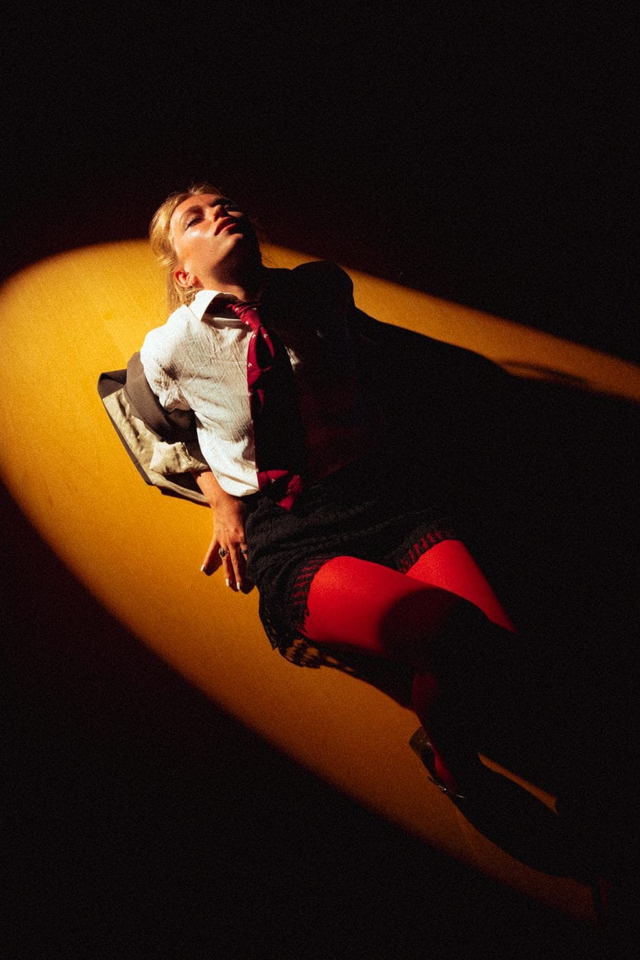 Silhouette prise dans un seul faisceau ambre sur fond noir, bottes rouges et coulée de lumière au sol, Amanda Black