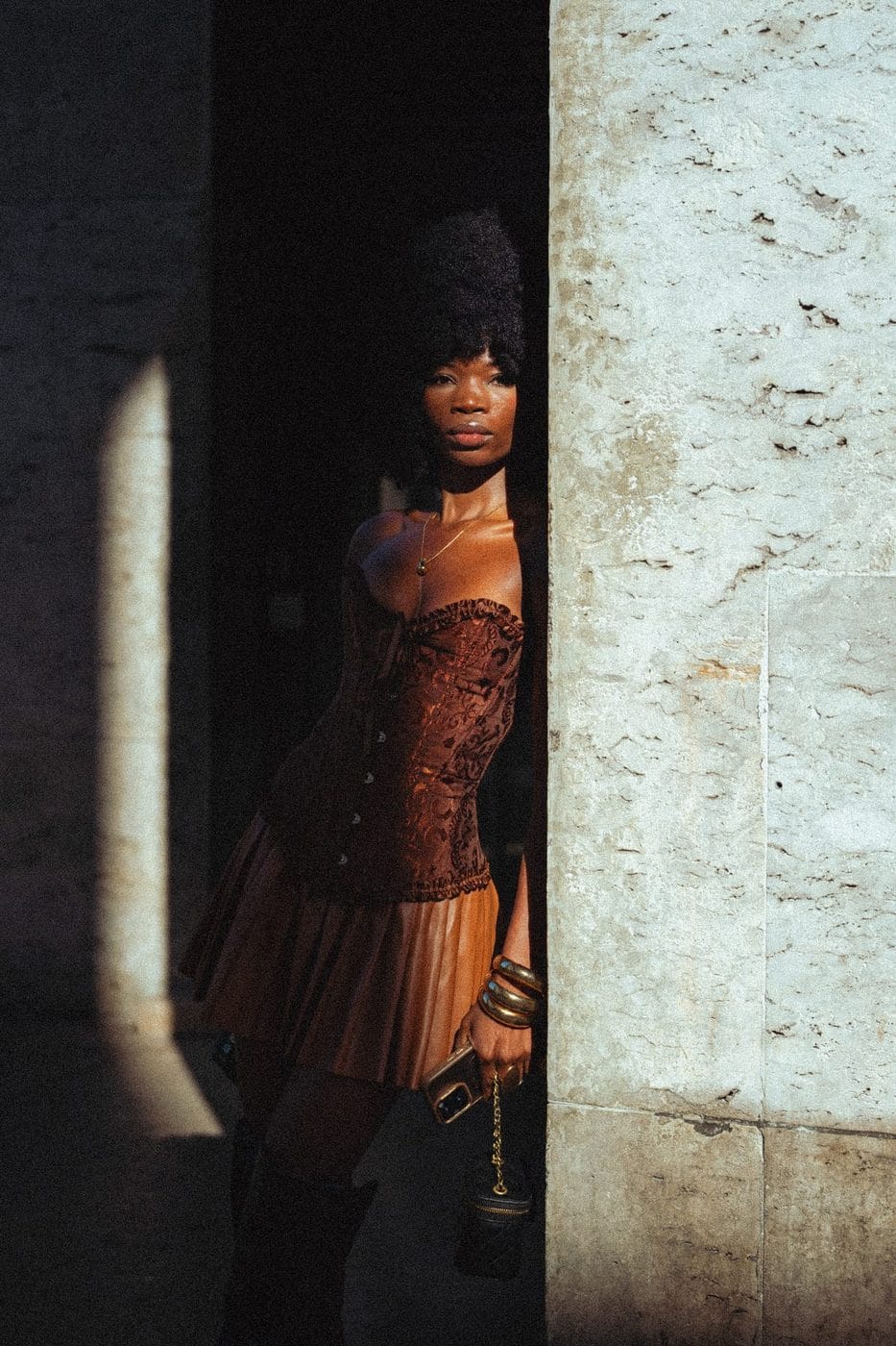 Femme en corset rouille dans un rai de lumière sur un mur de pierre, Zaila (@zaila_56)