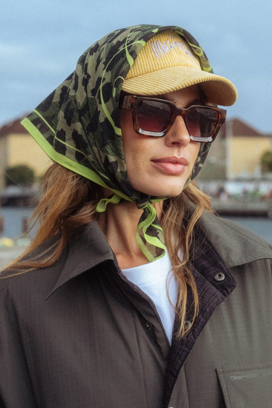 Portrait d'une femme en foulard léopard vert, casquette jaune et lunettes de soleil au bord de la Seine